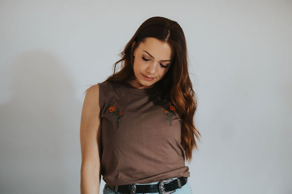 Woman looks down as she wears her Jackson Hole Wyoming lifestyle tank with the embroidered state flower on the chest
