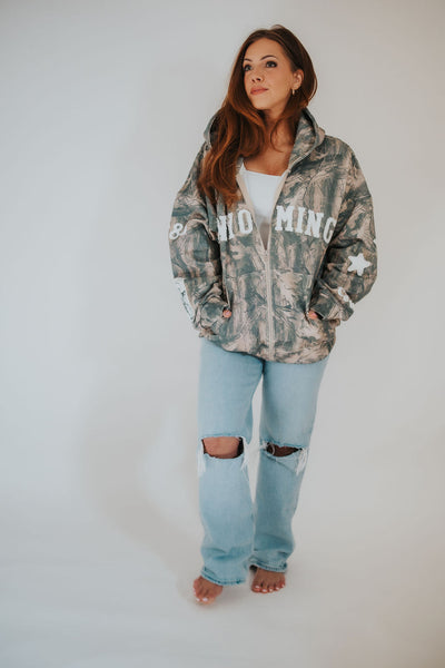 stylish woman places her hands in the pockets of her oversized, RUBY WYLD camo sweatshirt with embroidered detail 