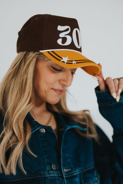 Woman smiles and looks down as she grams the brim of her licensed, unique 307 University of Wyoming hat with stars on the front 