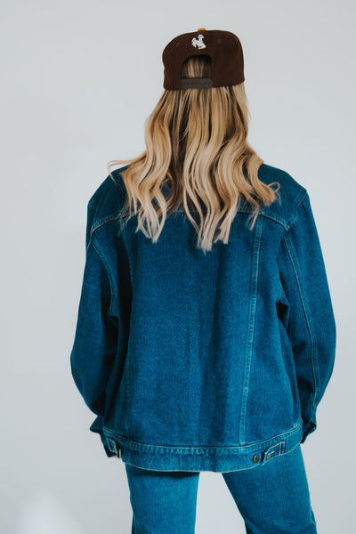 Woman poses to the back showing off her all denim classic western outfit and signature RUBY WYLD Steamboat snapback cap 