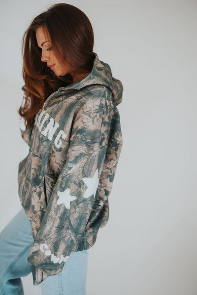 side profile of modern Wyoming cowgirl posing in RUBY WYLD's signature camo zip up hoodie 