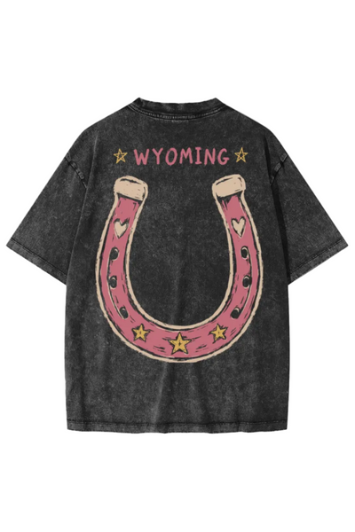 A dark gray acid-wash t-shirt shown from the back, featuring a large pink horseshoe graphic with gold stars and hearts, and the word 'WYOMING' printed in pink above it.