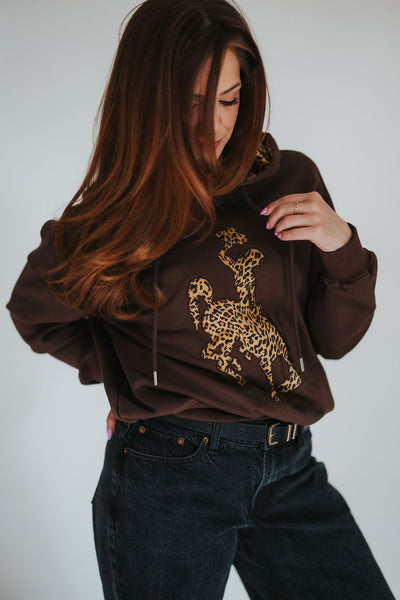 Woman grabs the strong her of her brown steamboat bucking horse hoodie with cheetah print detailing