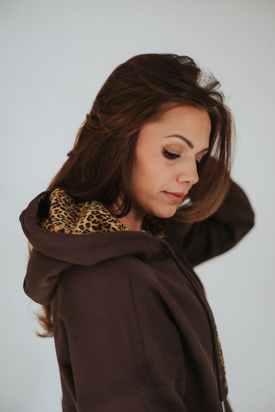 woman brushes her hair back and looks over her shoulder in a licensed women's University of Wyoming hoodie from RUBY WYLD with cheetah print lining the hood 