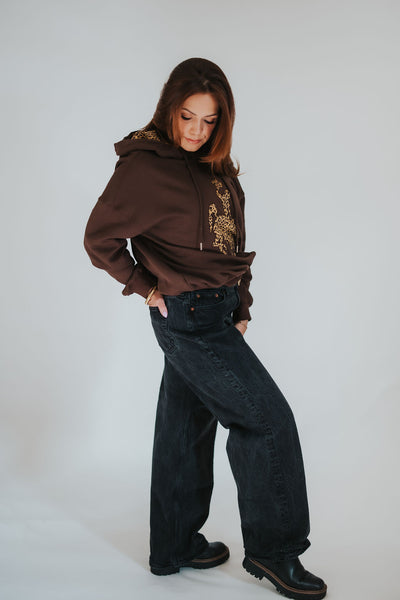 Woman pops her leg and poses to the side in her brown University of Wyoming bucking horse hoodie sweater