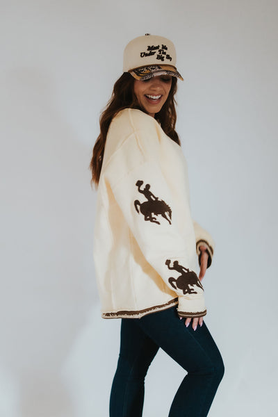 woman wearing RUBY WYLD's oversized butter yellow pullover sweater with Wyoming steamboat (cowboy on a bucking horse) on the sleeves