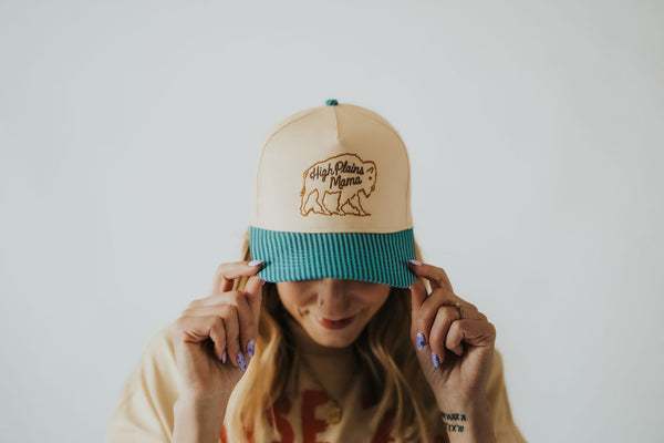 woman wears a beige and turquoise corduroy brimmed snapback hat with a Wyoming bison on the front 