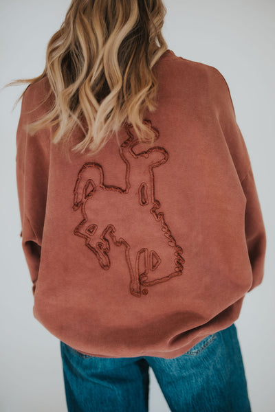 Woman shows off the University of Wyoming bucking horse patchwork on her oversized, vintage-style brown crewneck sweater