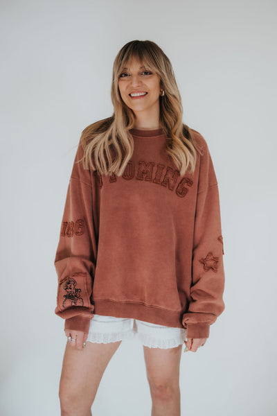 woman smiles and poses in a RUBY WYLD vintage-style crewneck with licensed University of Wyoming patchwork throughout