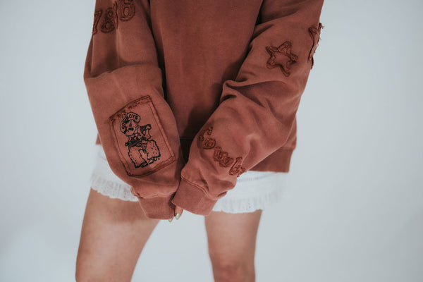 woman shows off the sleeves of her hand-designed RUBY WYLD crewneck with University of Wyoming Cowboys and Pistol Pete patchwork detailing