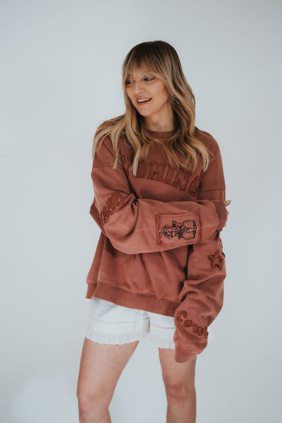 Fashionable woman styles an oversized, brown washed tonal crewneck with "Wyoming" patched on the chest and Pistol Pete and 1886 on the sleeves