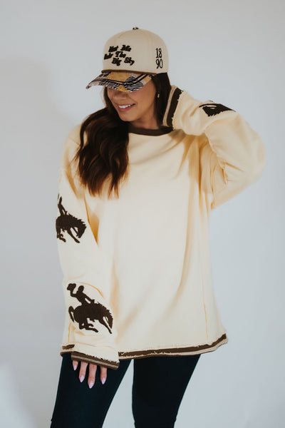 Person wearing a butter yellow-colored sweater with Wyoming bucking horse logos.
