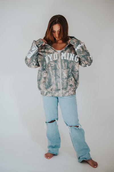 woman adjusts zip-up, vintage style University of Wyoming, Pistol Pete camo hoodie 