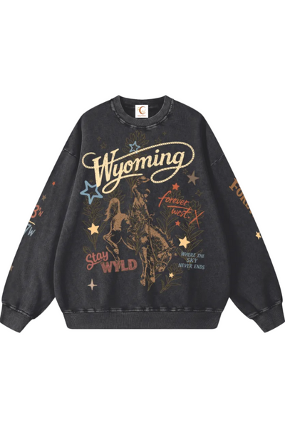 A dark gray washed crewneck sweatshirt featuring a vintage-style western graphic with a cowboy on a bucking horse, the word 'Wyoming' in large cream script, and gold and blue star accents, shown against a plain white background.