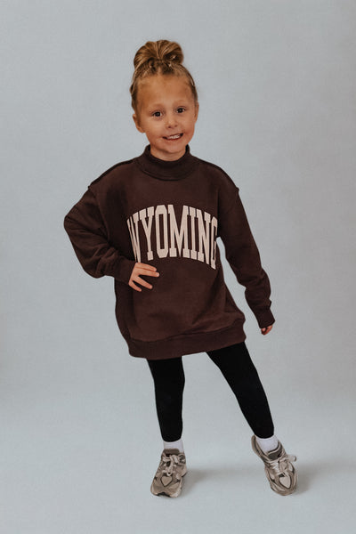 Child wearing a brown sweatshirt with 'WYOMING' printed on it against a plain background