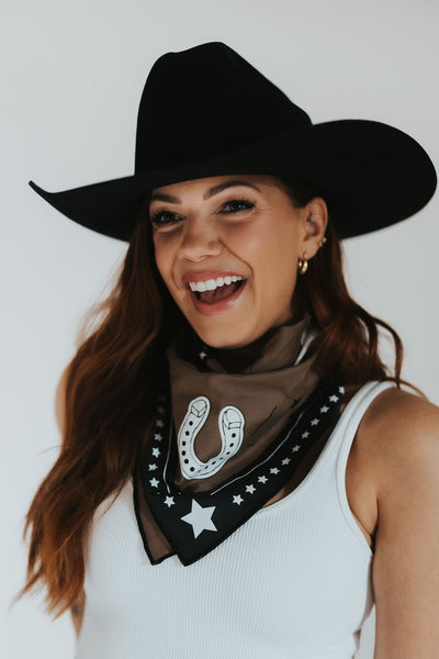 Modern Wyoming cowgirl smiles in a black cowboy hat as she wears her statement RUBY WYLD western bandana 