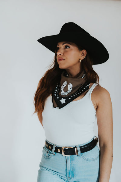Wyoming woman looks off into the distance in her black cowboy hat showing off her custom designed RUBY WYLD scarf with a horseshoe and stars on the front!