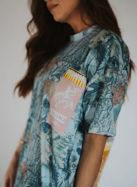 woman wearing an oversized camo short sleeve t-shirt with a "since 1886" Wyoming matchbook design on the front left pocket